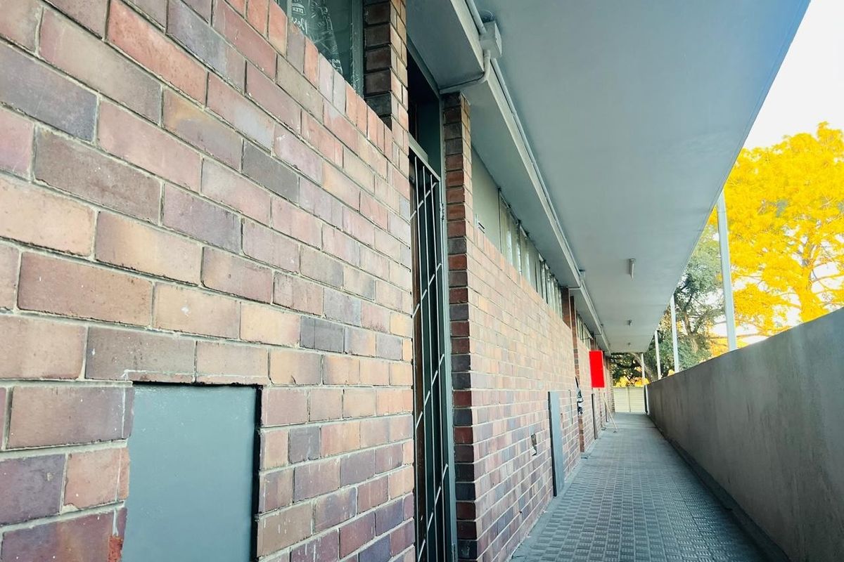 A view of the exterior rear walkway featuring brick wall construction, a security gate, and a covered paved path.