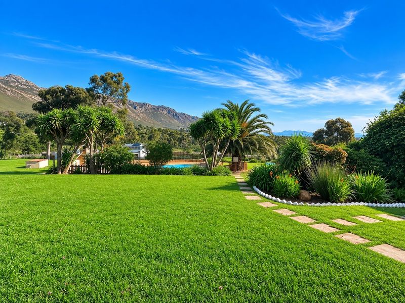 A beautifully maintained garden featuring a lush green lawn, stone paver pathway, and a swimming pool set against a scenic mountain backdrop.
