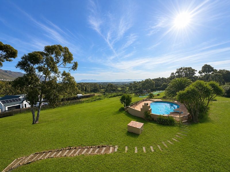 Aerial view of a landscaped garden featuring a swimming pool, stone pathway, and expansive scenic views of the surrounding landscape.