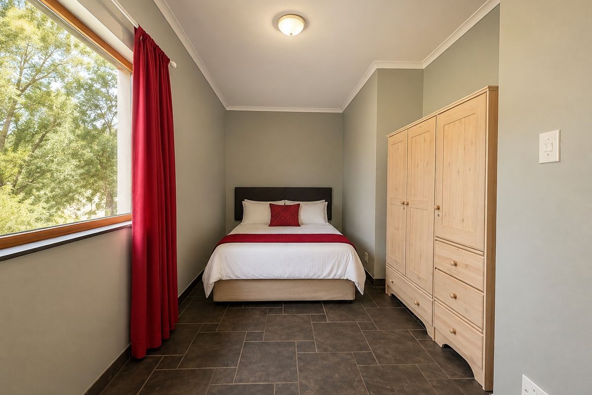 A well-maintained bedroom featuring tiled flooring, neutral wall tones, and a large window providing natural light and garden views.