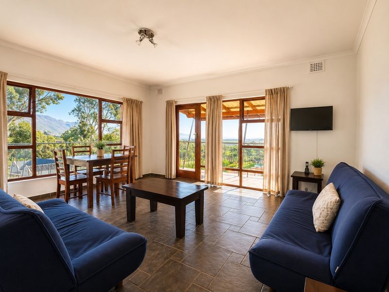 Bright open-plan living and dining area featuring tiled floors, large windows, and glass doors leading to a balcony with scenic views.