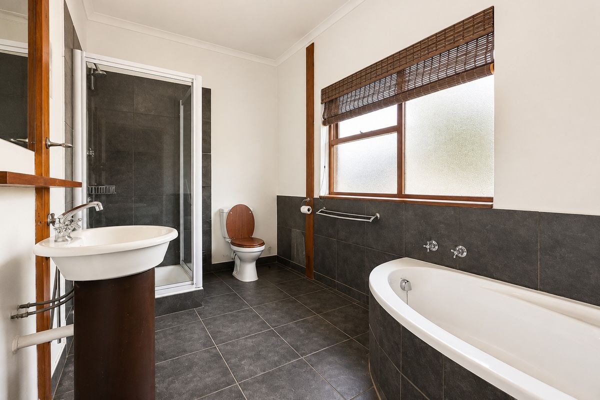 A well-maintained bathroom featuring a pedestal sink, a separate shower enclosure, and a built-in bathtub with dark tiled finishes.
