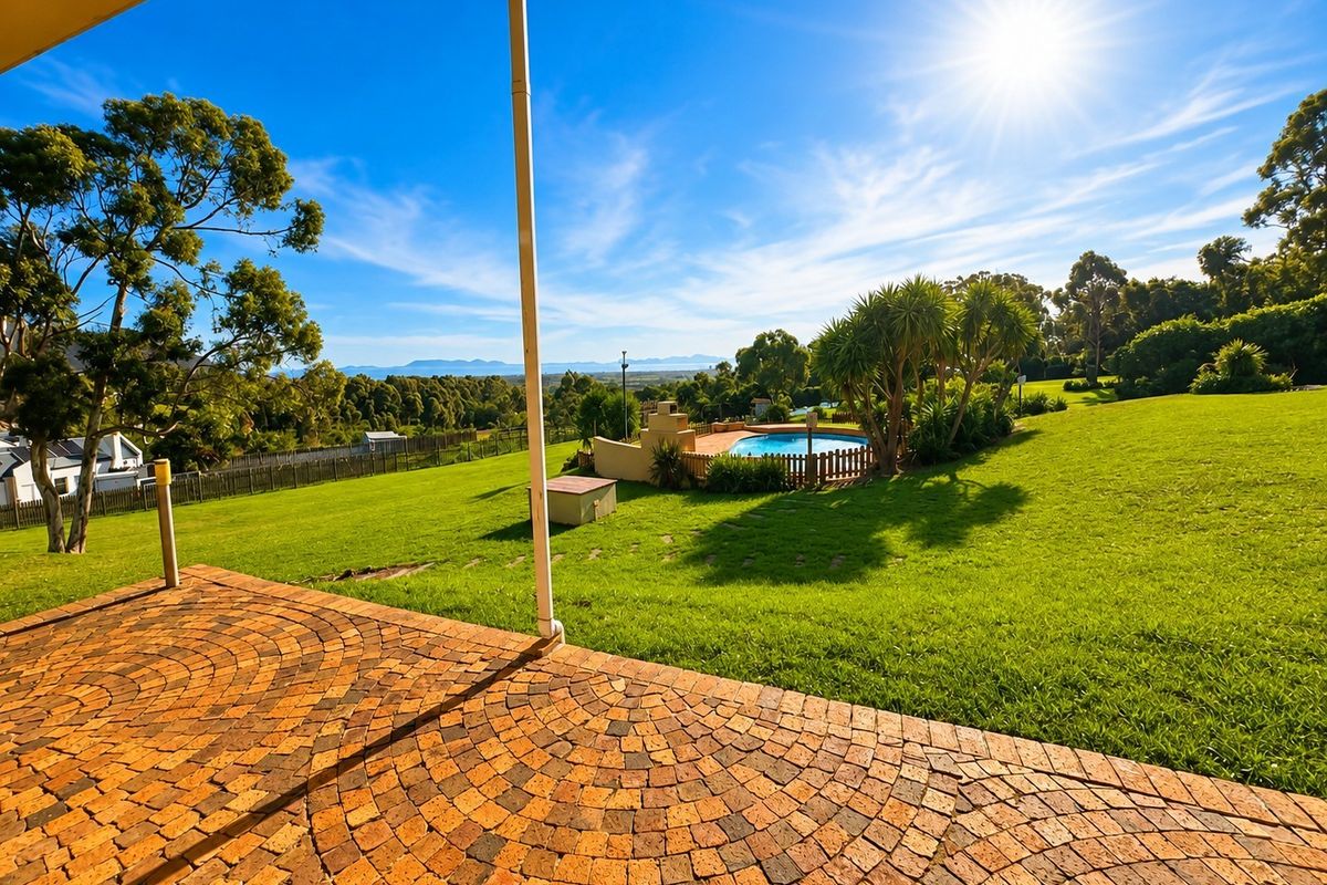 Spacious rear garden featuring a brick-paved patio, a swimming pool with fencing, and expansive lawn areas with scenic landscape views.