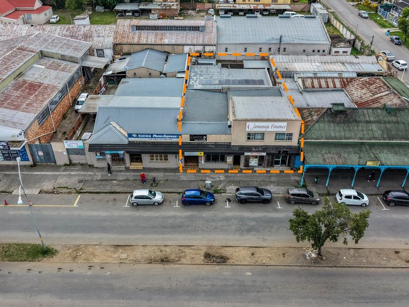 Aerial view of a commercial property block featuring multiple storefronts with corrugated metal roofing, situated along a street with public parking.