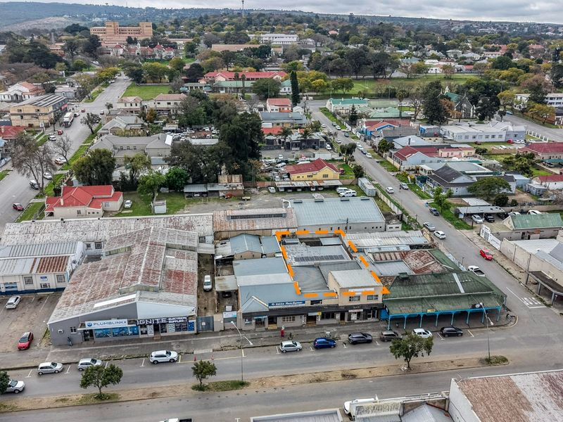 Aerial view of a commercial property block featuring multiple storefronts, metal roofing with solar panels, and street-level parking in a town setting.