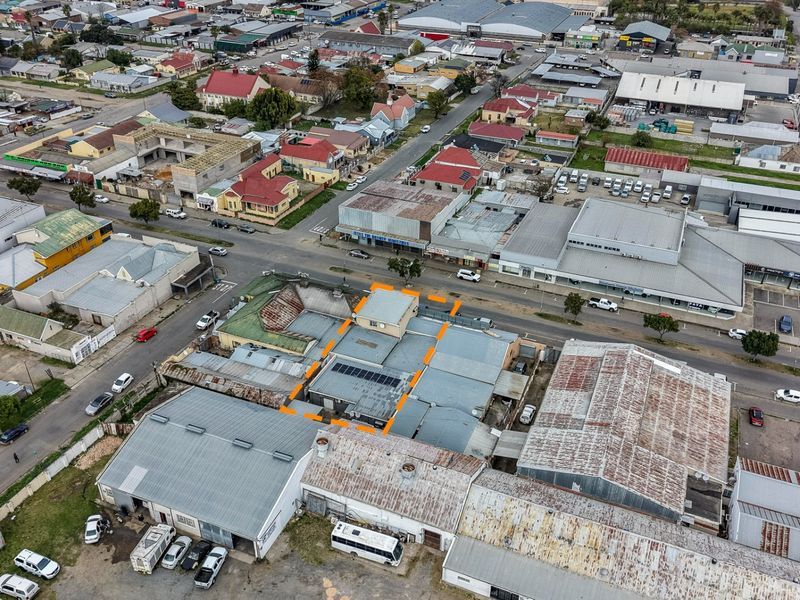 Aerial view of a commercial property featuring metal roofing and solar panels, situated within a dense urban business district.