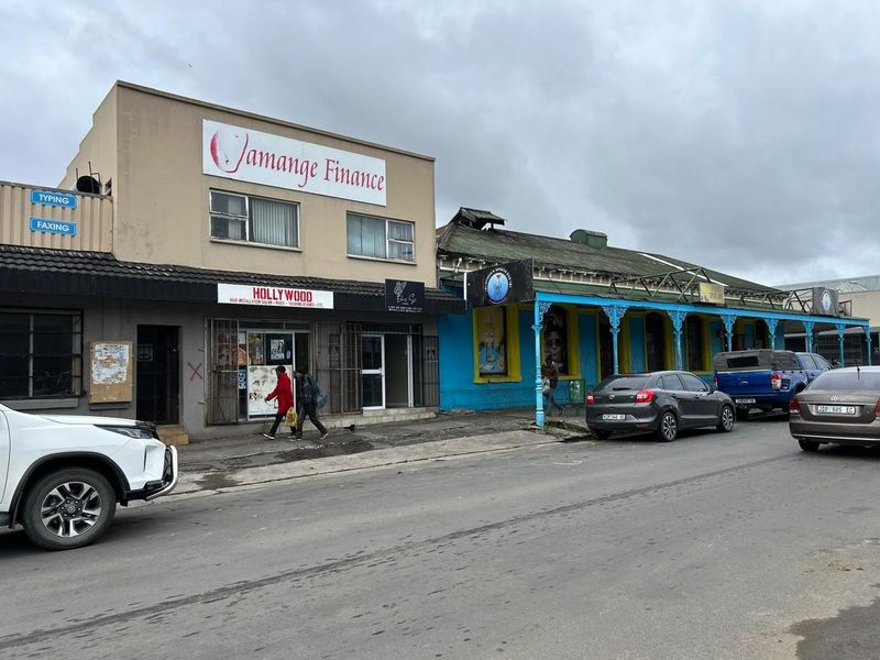 Street view of a commercial row featuring multiple storefronts with signage, security gates, and traditional architectural details along the sidewalk.