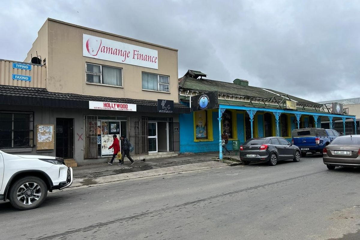 Street view of a commercial row featuring multiple storefronts with signage, security gates, and traditional architectural details along the sidewalk.