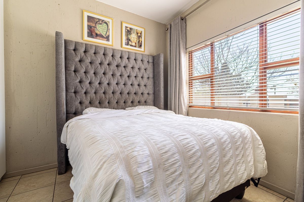 A cozy bedroom featuring tiled flooring, neutral wall finishes, and a window fitted with venetian blinds and curtains.