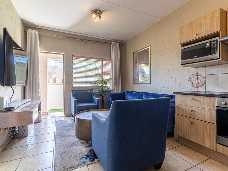 Open-plan living area featuring a compact kitchen with built-in cabinetry, integrated oven, and microwave, leading to a small balcony with tiled flooring.