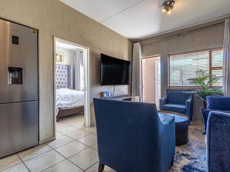 A living area featuring textured walls and tiled flooring, with an adjacent bedroom visible through the doorway.