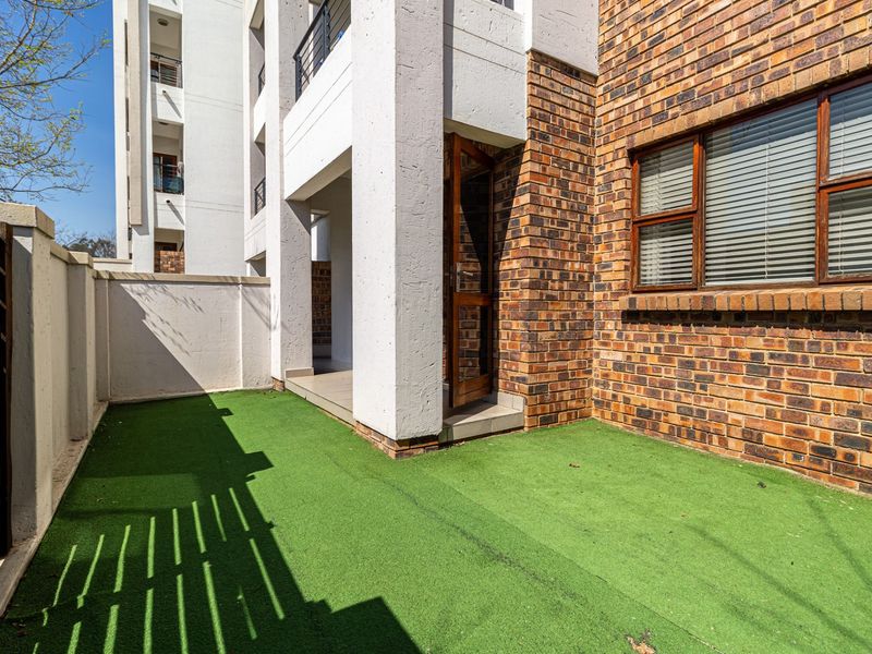 A private ground floor courtyard area featuring artificial grass, brick and concrete exterior finishes, and direct access to the apartment.