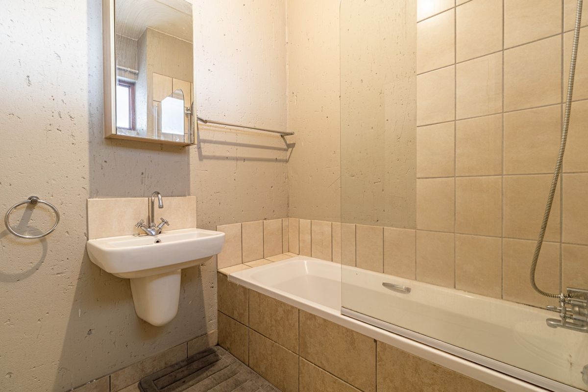 A functional bathroom featuring a pedestal basin, bathtub with a glass shower screen, and tiled wall finishes.