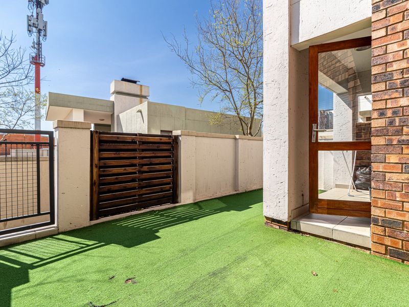 A private outdoor patio area featuring artificial grass, a brick facade, and a secure timber gate, providing a functional space for outdoor relaxation.