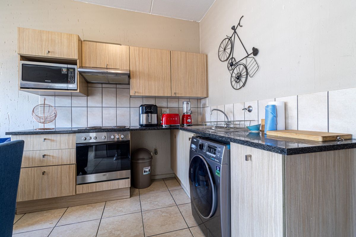 Compact kitchen featuring laminate cabinetry, granite countertops, built-in oven, extractor fan, and integrated microwave with tiled backsplash and flooring.