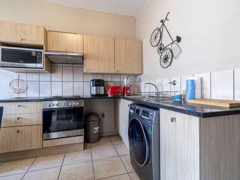 Compact kitchen featuring laminate cabinetry, granite countertops, built-in oven, extractor fan, and integrated microwave with tiled backsplash and flooring.