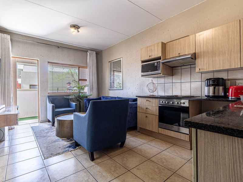 Open-plan living area featuring a compact kitchen with built-in cabinetry, granite countertops, and integrated appliances, leading to a small balcony.