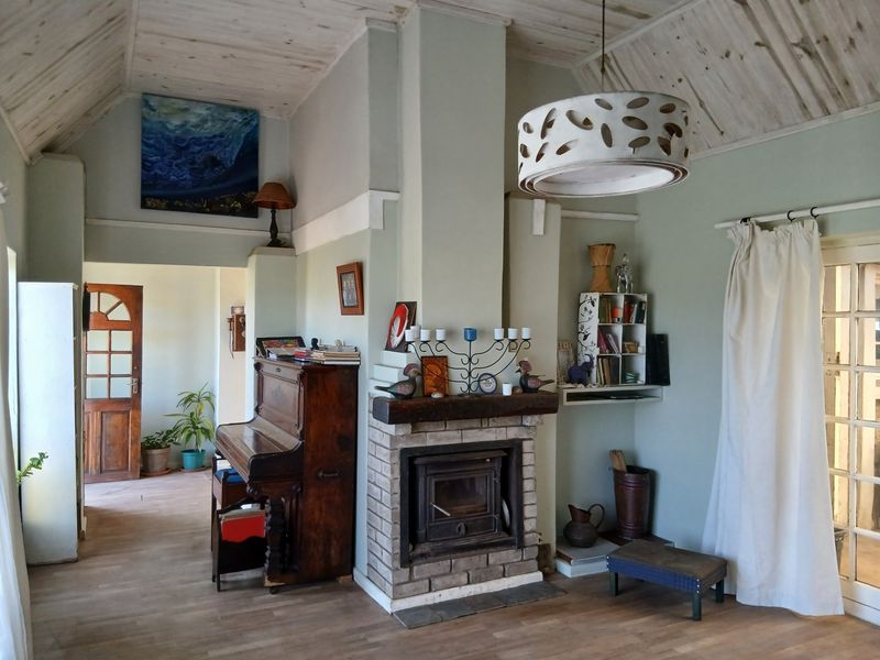 A cozy living room featuring a central brick fireplace, vaulted timber ceilings, and laminate flooring, with access to adjacent rooms via timber doors.