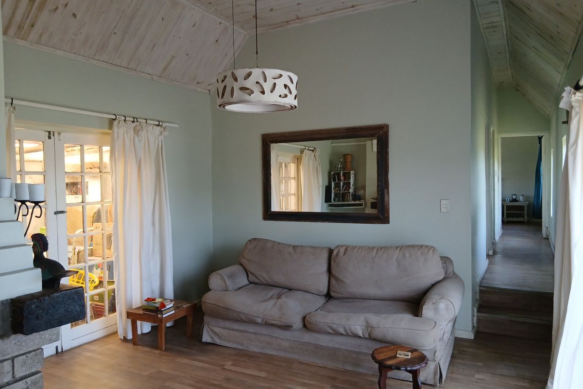 A cozy living room featuring a vaulted timber ceiling, laminate flooring, and a brick fireplace, with french doors leading to an adjacent space.