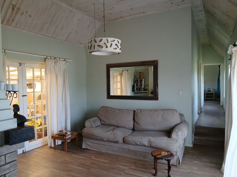 A cozy living room featuring a vaulted timber ceiling, laminate flooring, and a brick fireplace, with french doors leading to an adjacent space.