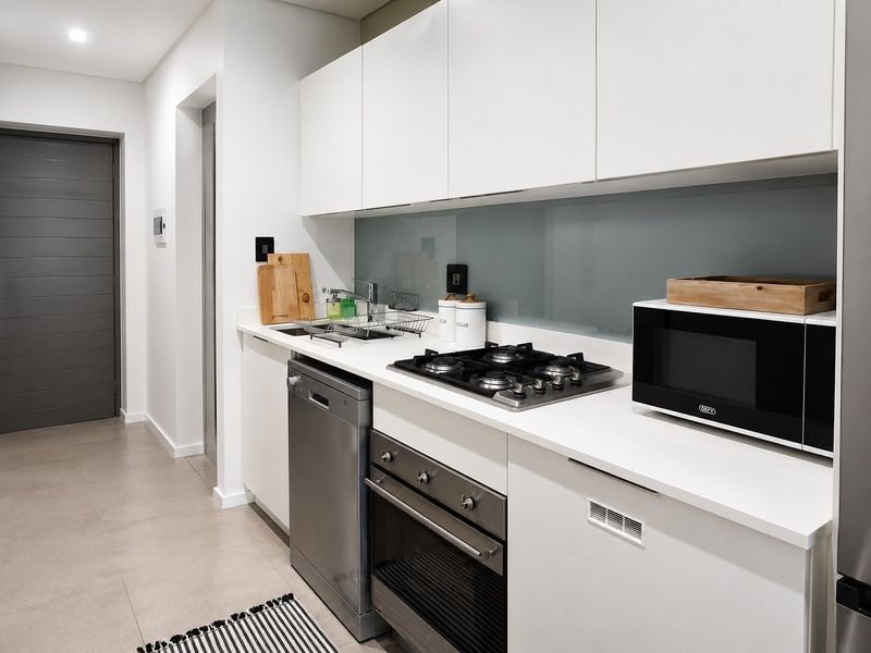 Modern kitchen featuring sleek white cabinetry, stone countertops, a glass splashback, and high-quality built-in appliances including a gas hob and oven.