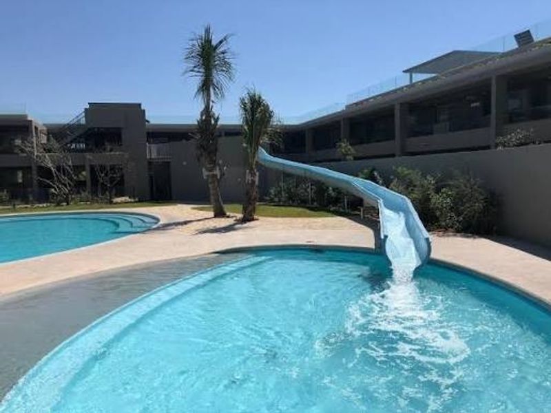 A well-maintained outdoor swimming pool area featuring a built-in water slide and paved surround, set within a modern residential complex.