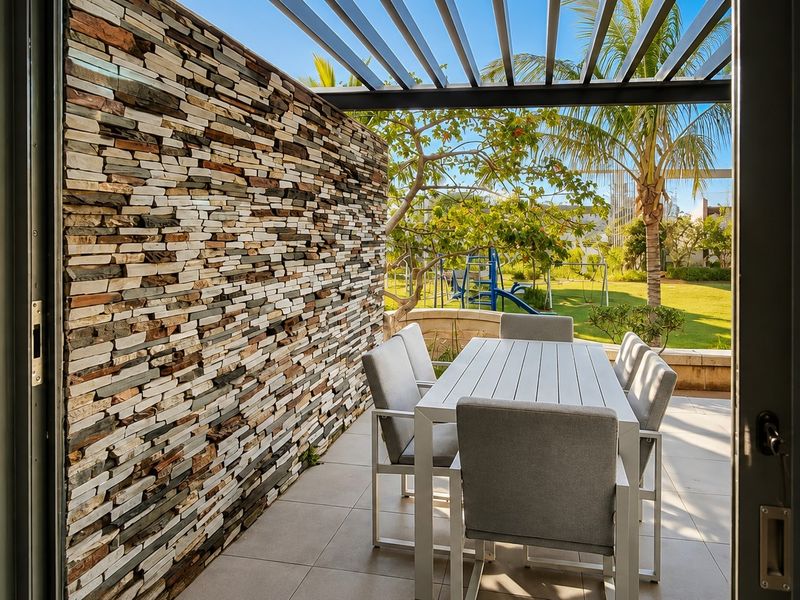 A modern covered patio featuring a striking stone feature wall, pergola overhead, and tiled flooring, offering a seamless transition to the garden area.