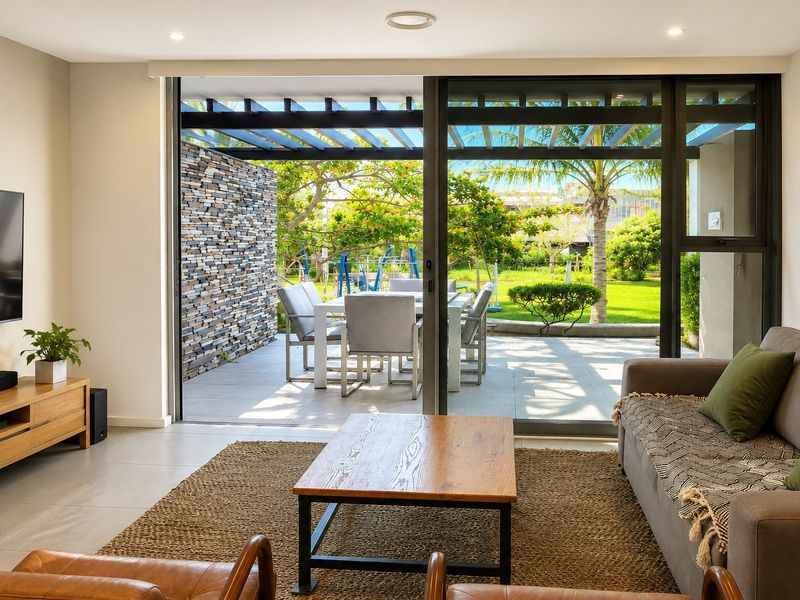 Modern living room featuring large sliding glass doors that open onto a paved patio with a pergola and stone feature wall.