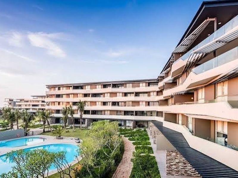A modern multi-story residential complex featuring expansive balconies, landscaped gardens, and a swimming pool area.