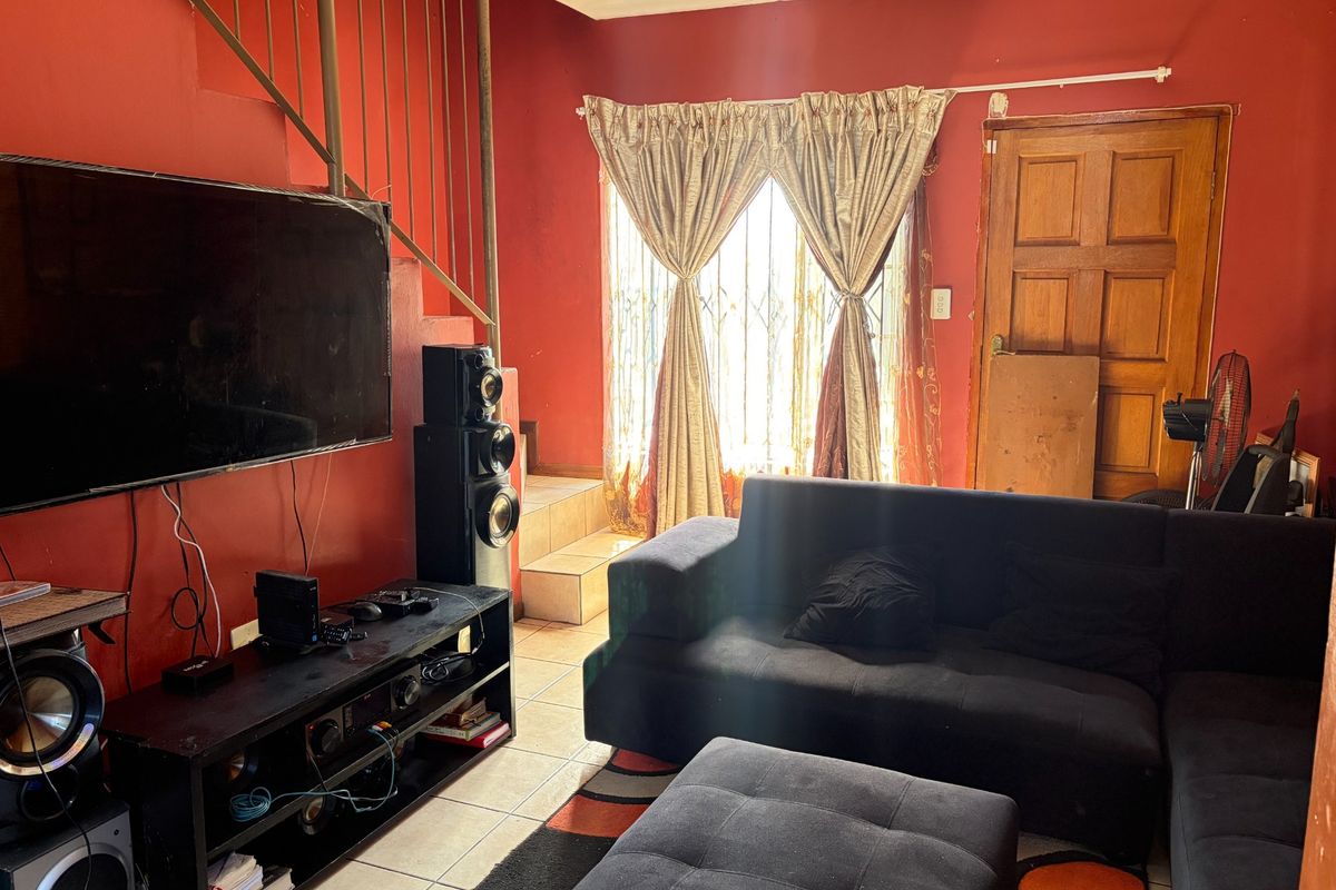 A living room featuring tiled flooring, a staircase, and a timber door, with red wall finishes.