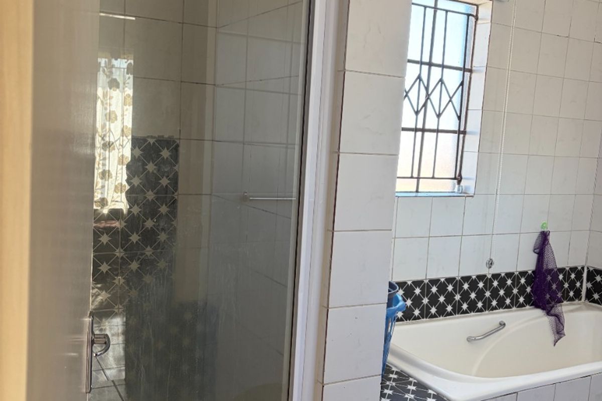A dated bathroom featuring a built-in bathtub, a separate shower enclosure, and tiled finishes, requiring cosmetic updates to modernize the space.