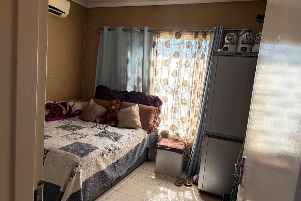 A compact bedroom featuring tiled flooring and a wall-mounted air conditioning unit, offering a functional space with potential for cosmetic updates.