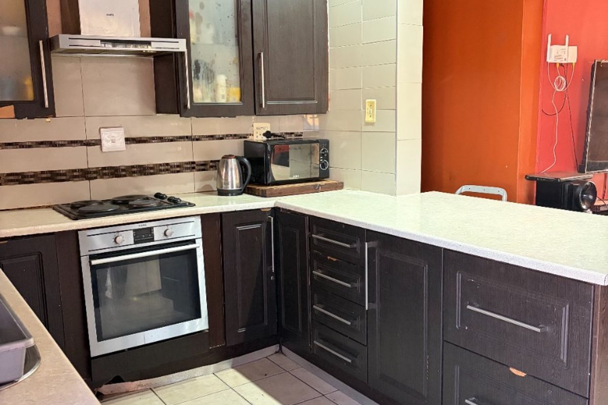 A functional kitchen featuring dark wood cabinetry, light countertops, built-in oven, gas hob, and tiled flooring with recessed lighting.