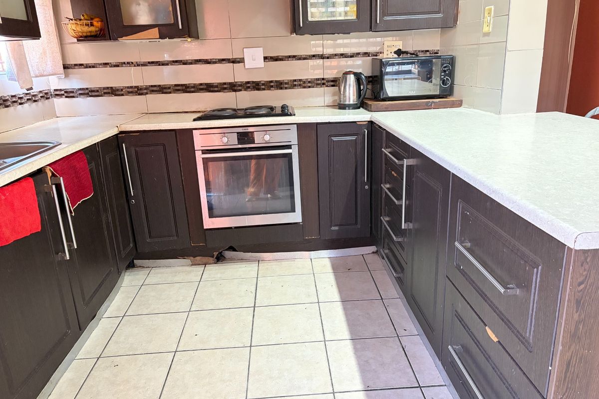 A functional kitchen featuring dark wood-finish cabinetry, tiled flooring, and built-in oven and hob, showing signs of wear and tear.