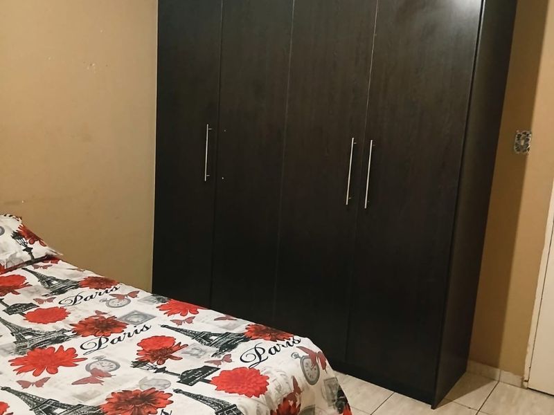 A bedroom featuring tiled flooring and a large dark wood built-in wardrobe.