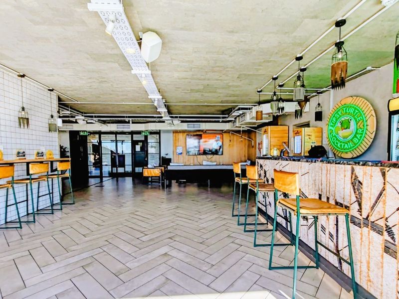 A commercial-style bar area featuring herringbone tile flooring, a built-in bar counter, and exposed industrial-style ceiling infrastructure.