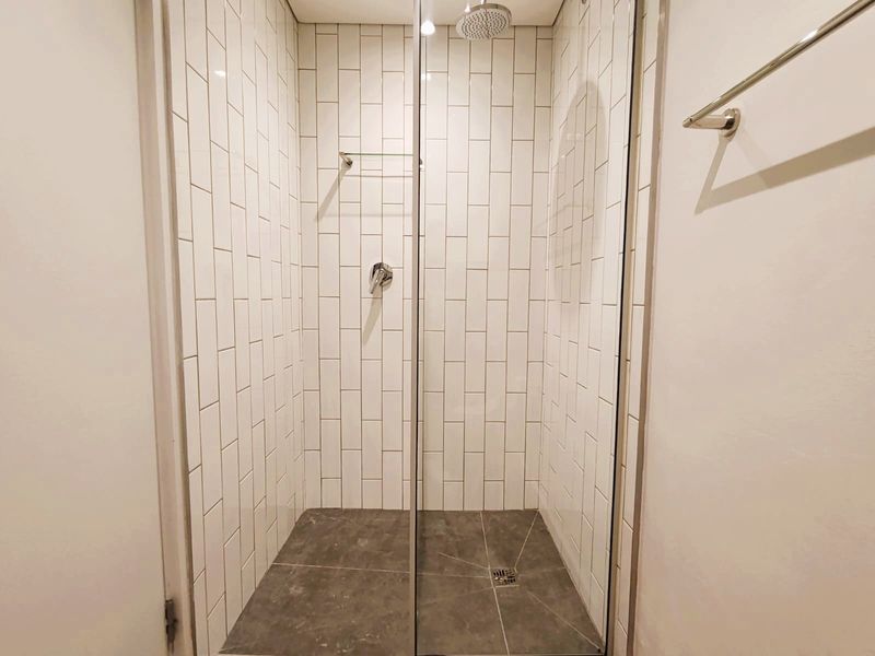 A modern, clean walk-in shower featuring white subway wall tiles, a rain shower head, and dark stone-look floor tiles with a glass screen.