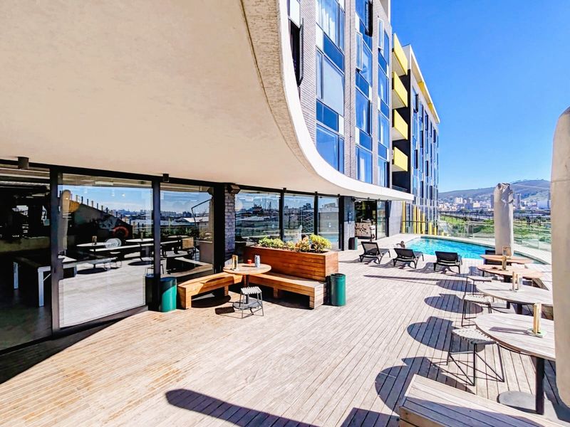 Outdoor pool area featuring timber decking, built-in bench seating, and a glass balustrade overlooking the city skyline.