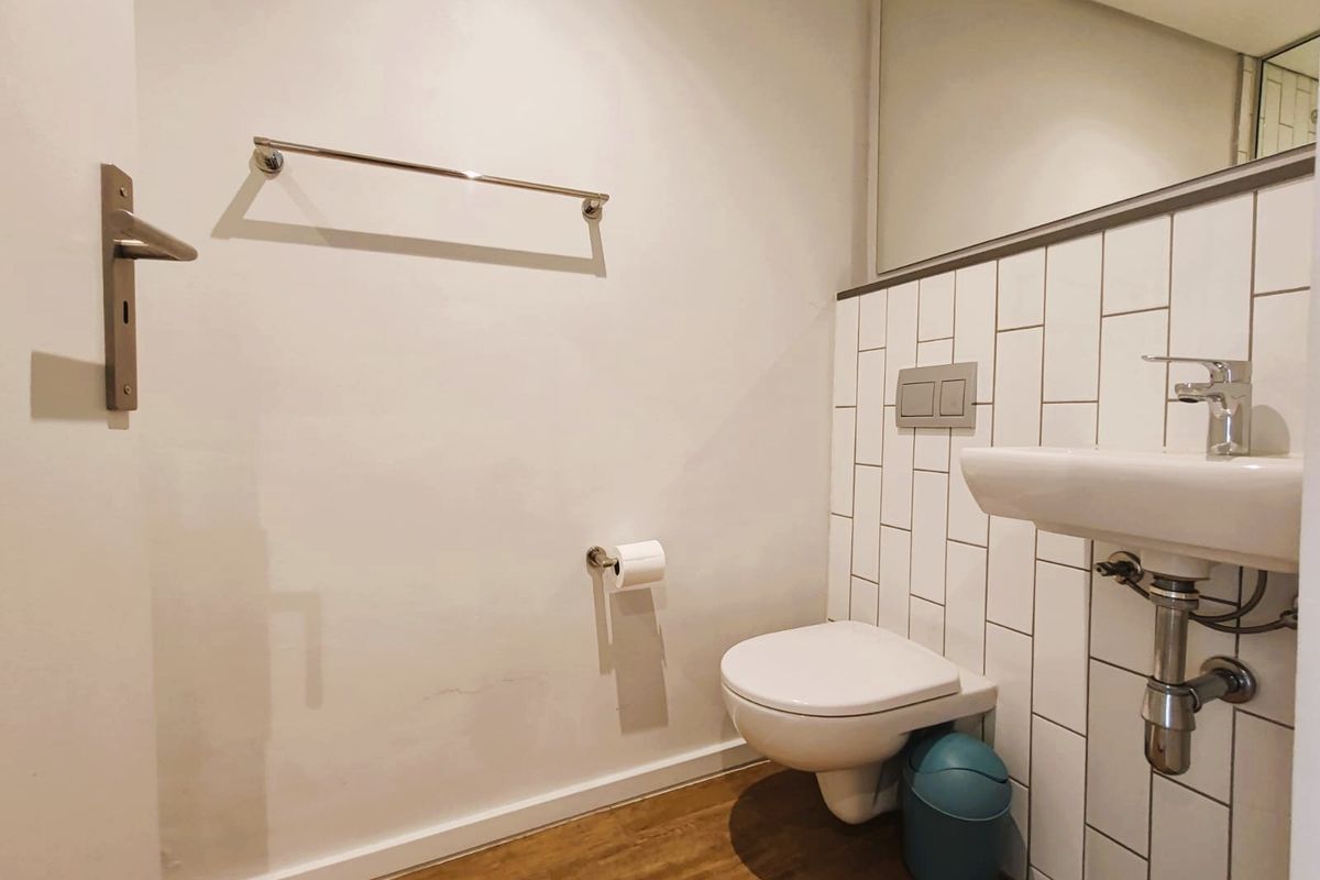 A clean, modern bathroom featuring a wall-mounted toilet, basin with chrome fixtures, subway tile backsplash, and wood-look flooring.