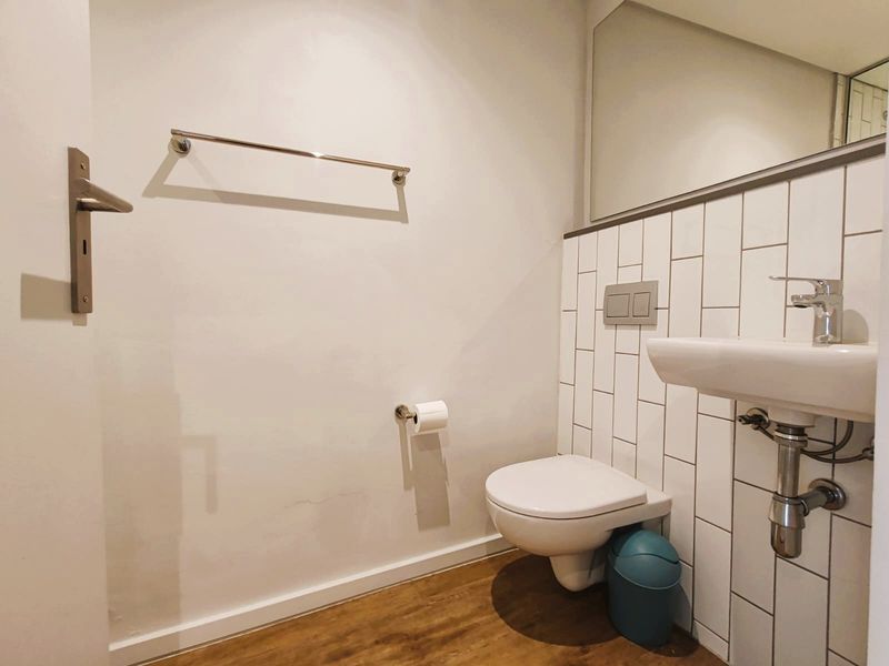 A clean, modern bathroom featuring a wall-mounted toilet, basin with chrome fixtures, subway tile backsplash, and wood-look flooring.