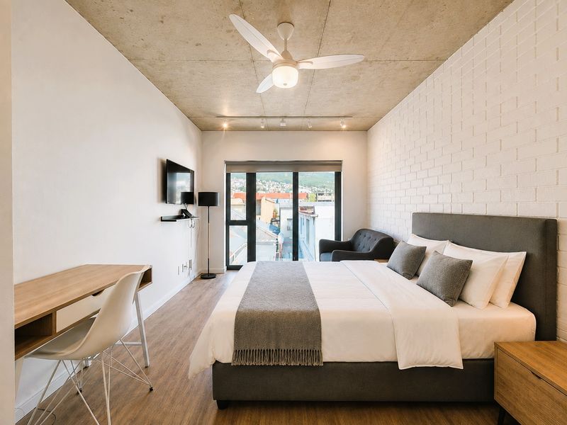 Modern bedroom featuring an exposed concrete ceiling, white brick feature wall, ceiling fan, and sliding glass doors leading to an outdoor area.