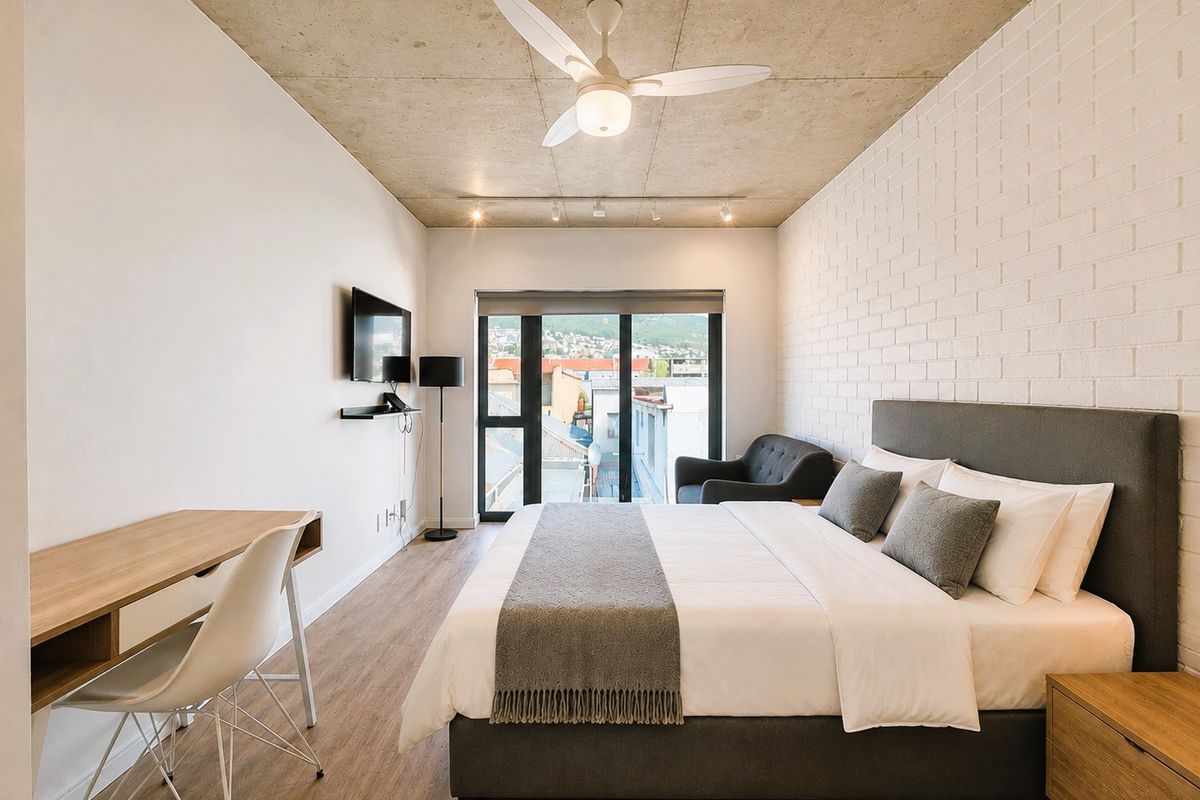 Modern bedroom featuring an exposed concrete ceiling, white brick feature wall, ceiling fan, and sliding glass doors leading to an outdoor area.
