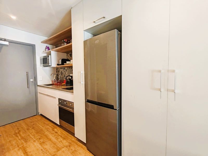 Compact modern kitchen featuring sleek white cabinetry, stainless steel oven, integrated fridge space, and stylish tiled backsplash with open shelving.