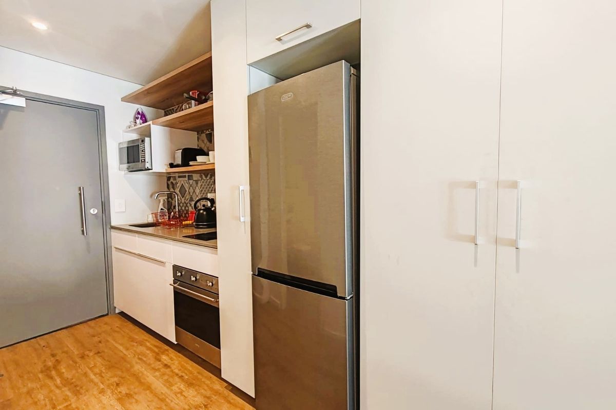 Compact modern kitchen featuring sleek white cabinetry, stainless steel oven, integrated fridge space, and stylish tiled backsplash with open shelving.