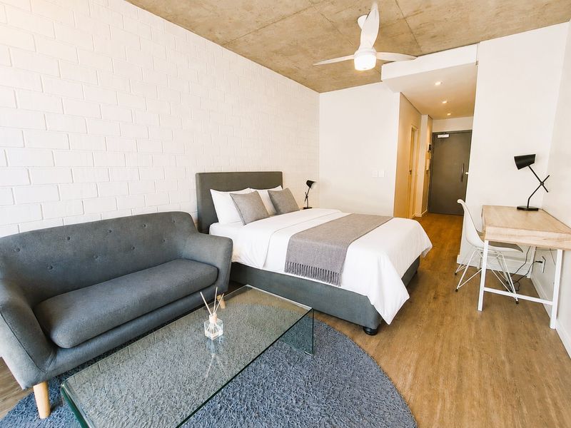A modern studio bedroom featuring an exposed concrete ceiling, white brick feature wall, and laminate flooring, creating a contemporary and industrial-inspired living space.
