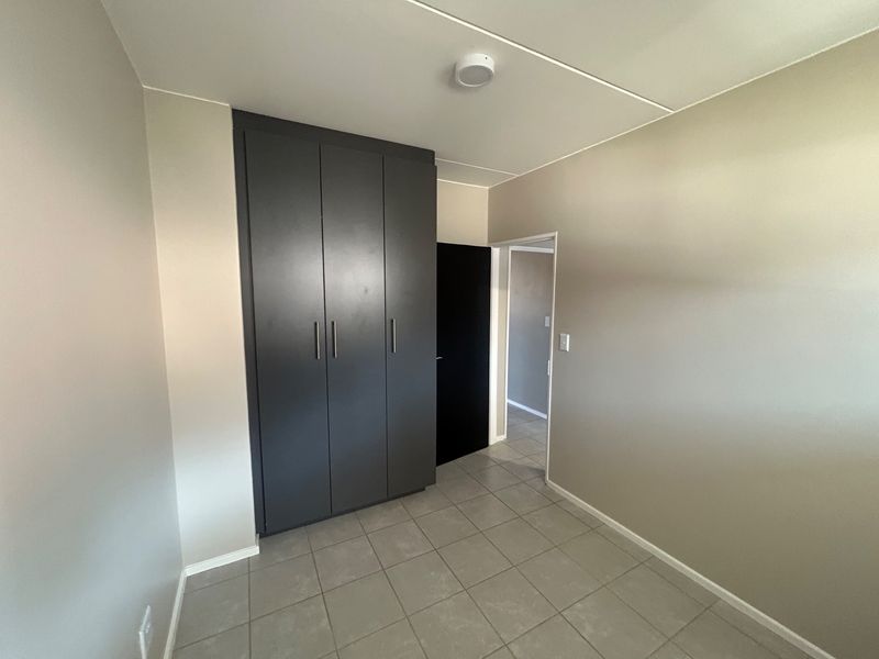 A clean, empty bedroom featuring modern dark built-in cupboards, neutral wall paint, and grey tiled flooring.