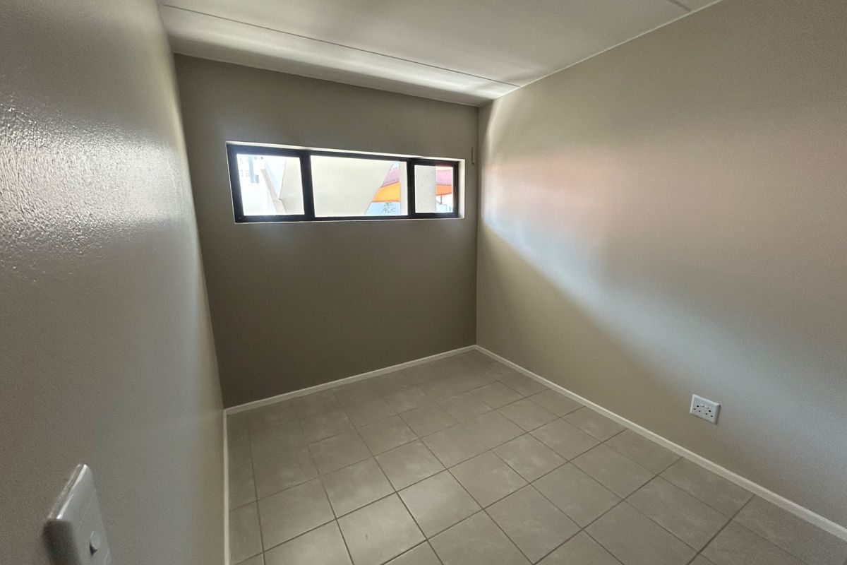 A clean, empty bedroom featuring neutral wall paint, tiled flooring, and a horizontal window providing natural light.