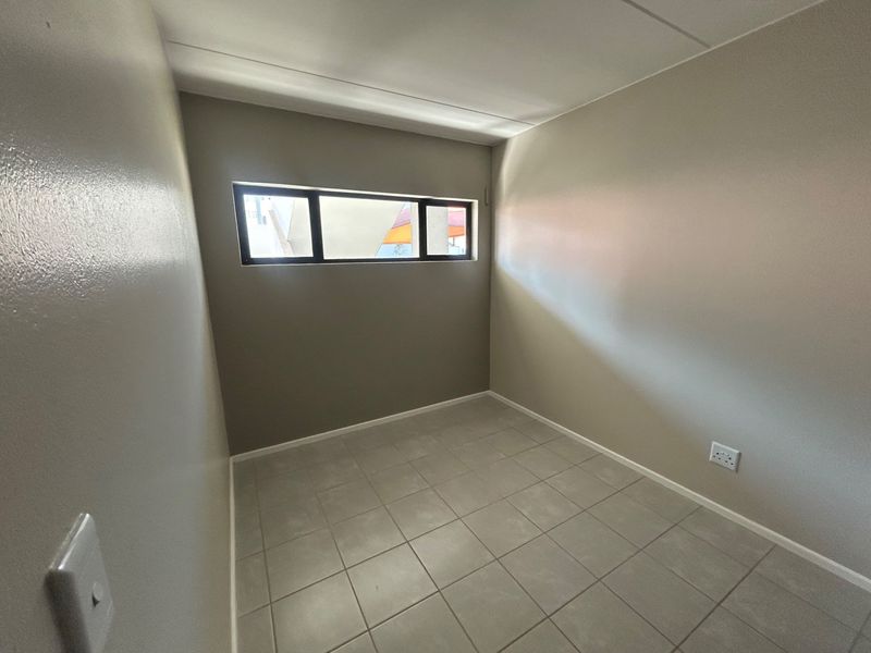 A clean, empty bedroom featuring neutral wall paint, tiled flooring, and a horizontal window providing natural light.
