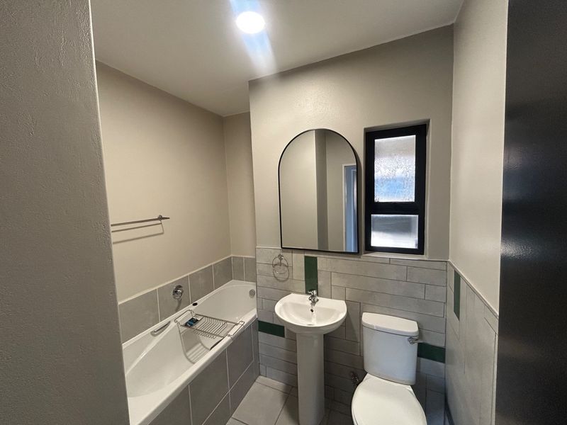 A clean, modern bathroom featuring a pedestal basin, bathtub, toilet, and stylish arched mirror with neutral wall finishes and tiled splashbacks.