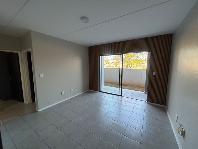 An empty living room featuring neutral tiled flooring, modern timber slat wall accents, and a sliding glass door providing access to an outdoor patio area.